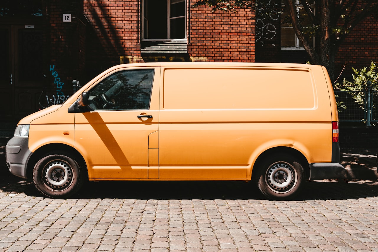 Ein Transporter ohne Beschriftung steht auf Kopfsteinpflaster vor der Backsteinfassade eines Altbaus.